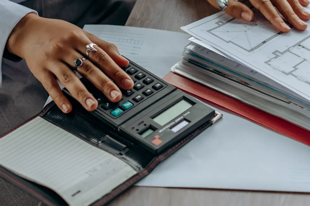 Stock photograph: hands using a calculator beside building plans, representing energy audit calculations